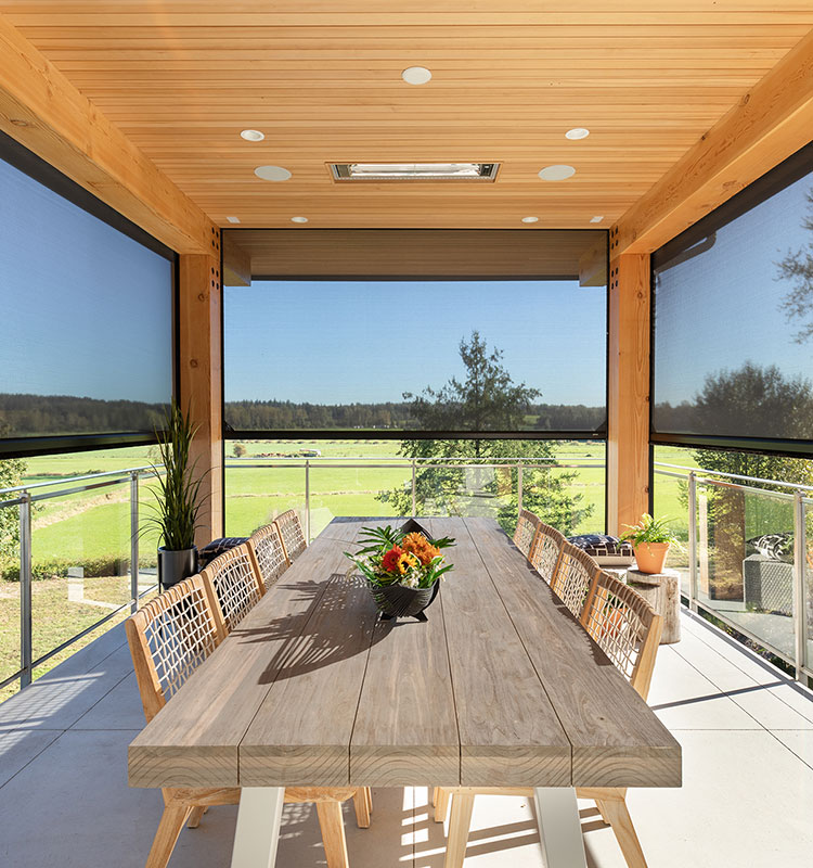 Véranda couverte avec moustiquaires motorisées et table à manger en bois, surplombant un paysage verdoyant à travers des garde-corps en verre