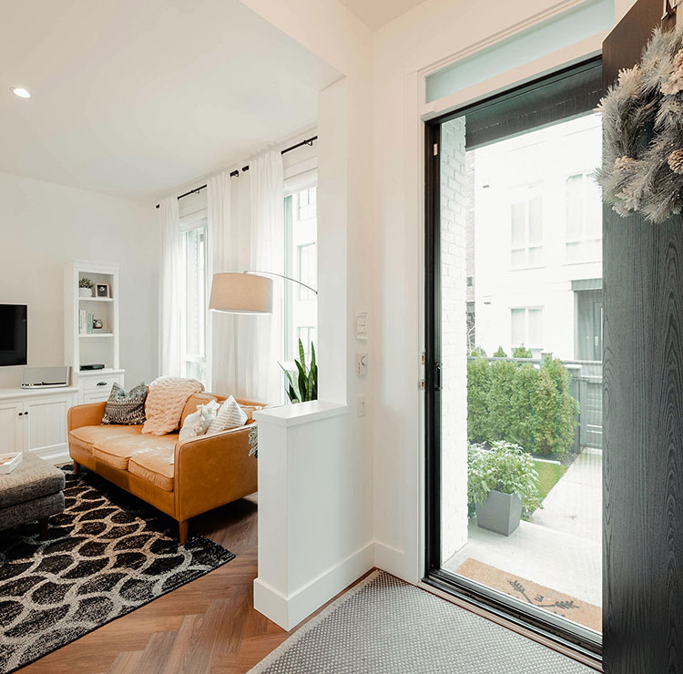 Entrée de maison moderne avec une porte d'entrée noire et une moustiquaire rétractable presque invisible sur la porte ouverte.