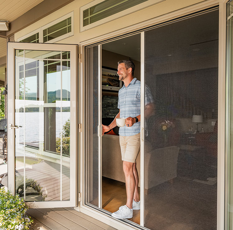 Homme debout dans l'embrasure tenant un café, avec une moustiquaire rétractable tirée sur l'entrée du patio.