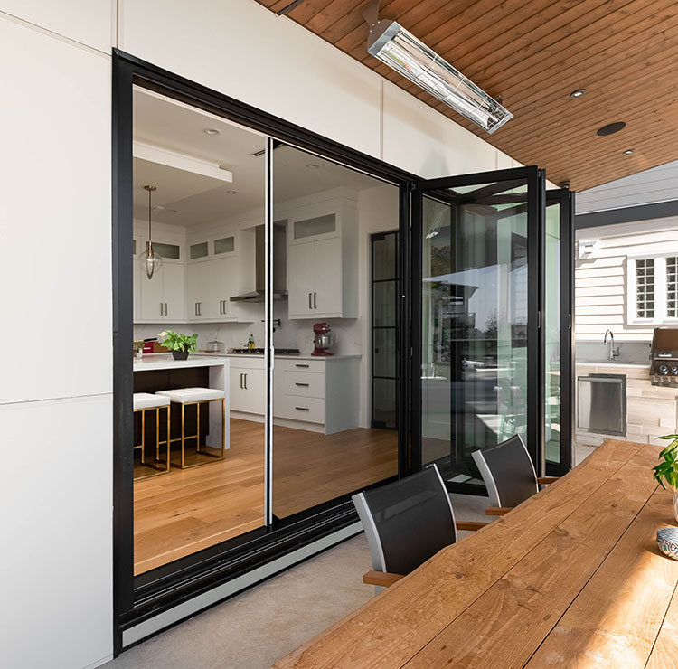 Cuisine intérieure-extérieure avec portes vitrées pliantes à cadre noir avec moustiquaires rétractables et table à manger en bois