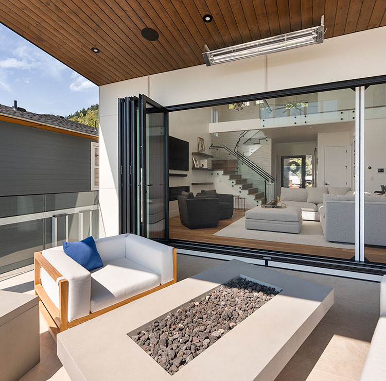 Balcon moderne avec système de porte vitrée pliante, canapé d'extérieur blanc et foyer intégré en pierre