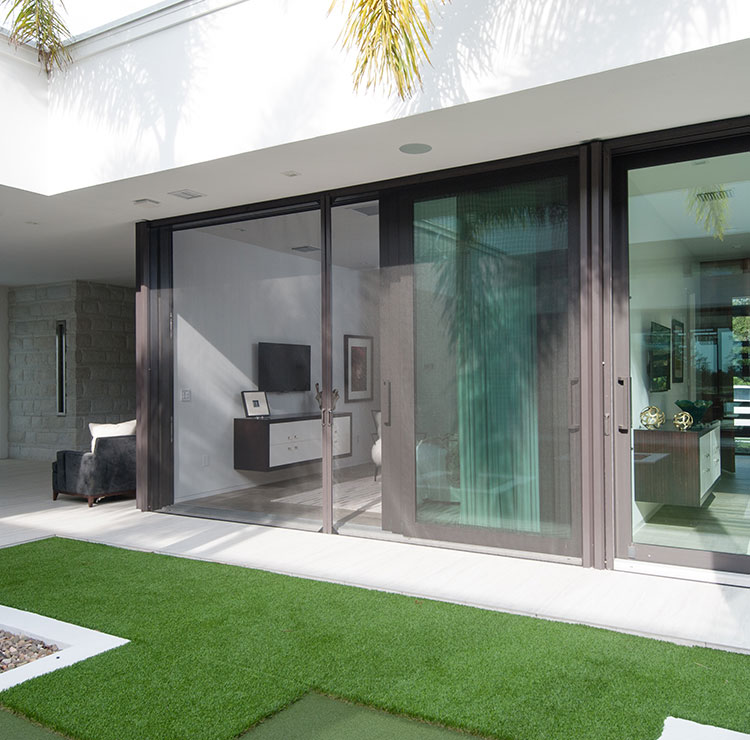 Patio tropical moderne avec grandes portes vitrées coulissantes, gazon artificiel et palmiers encadrant l'espace