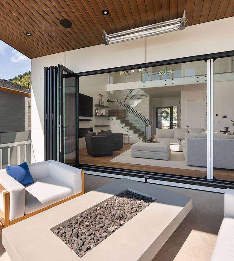 Patio couvert moderne avec portes vitrées pliantes, mobilier d'extérieur blanc et foyer intégré donnant sur un salon contemporain