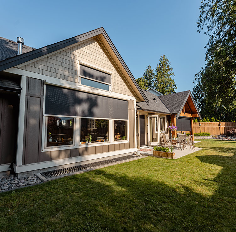 Extérieur de maison artisanale moderne avec grande fenêtre équipée d'un store solaire extérieur et système de guide-câble, entourée d'un jardin paysager avec des conifères