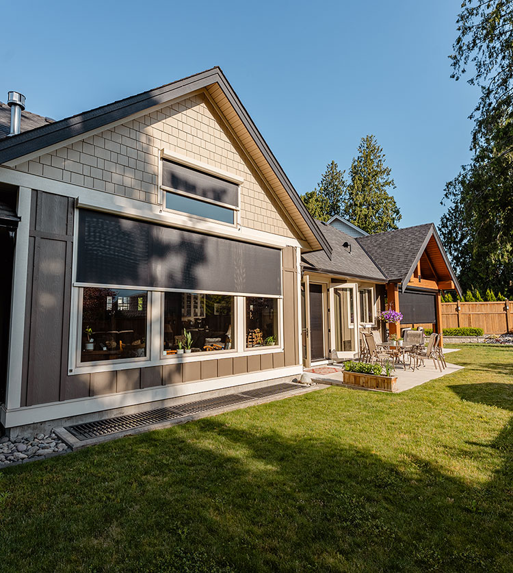 Extérieur de maison artisanale moderne avec grande fenêtre équipée d'un store solaire extérieur et système de guide-câble, entourée d'un jardin paysager avec des conifères