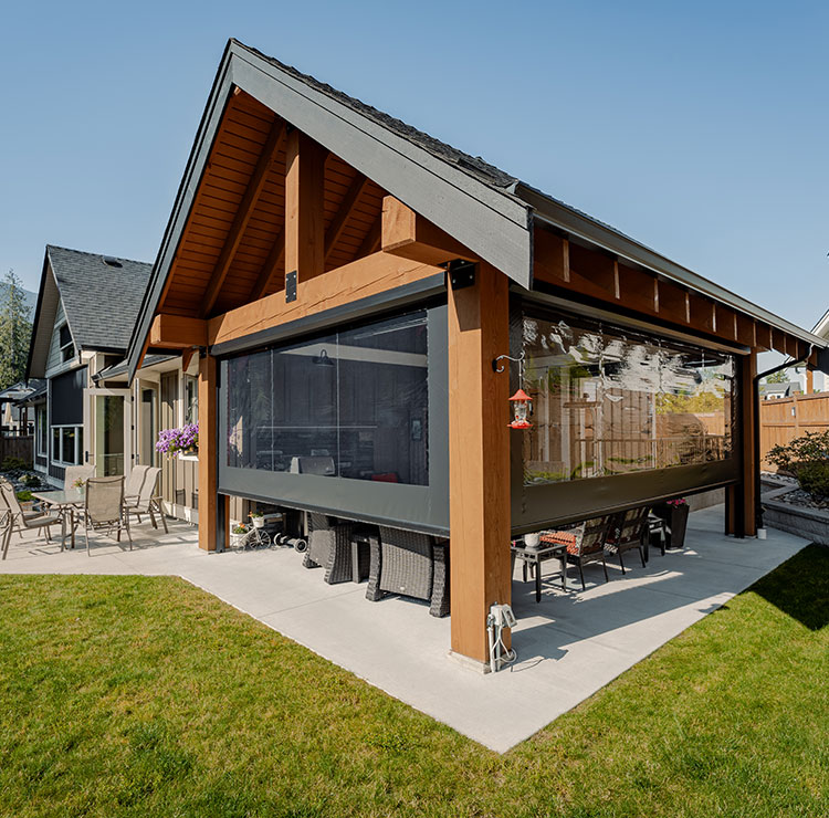 Pergola à ossature bois avec écrans rétractables créant un espace de vie extérieur abrité, présentant des meubles en osier