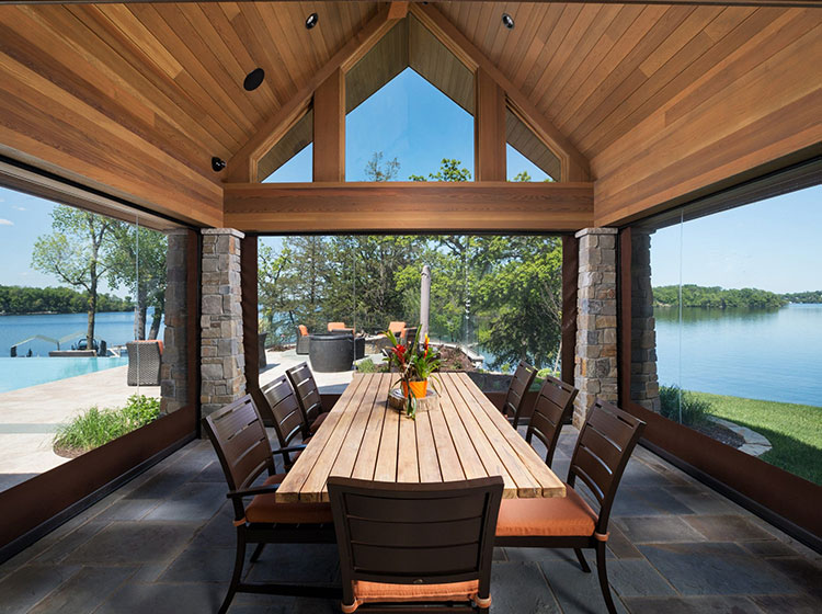 Pavillon de repas au bord du lac avec moustiquaires rétractables, plafond en bois et colonnes en pierre surplombant la vue sur l'eau