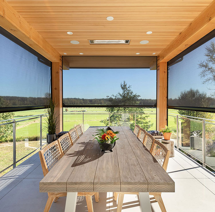 Espace repas couvert avec table en bois et moustiquaires motorisées, offrant des vues panoramiques sur le paysage vert