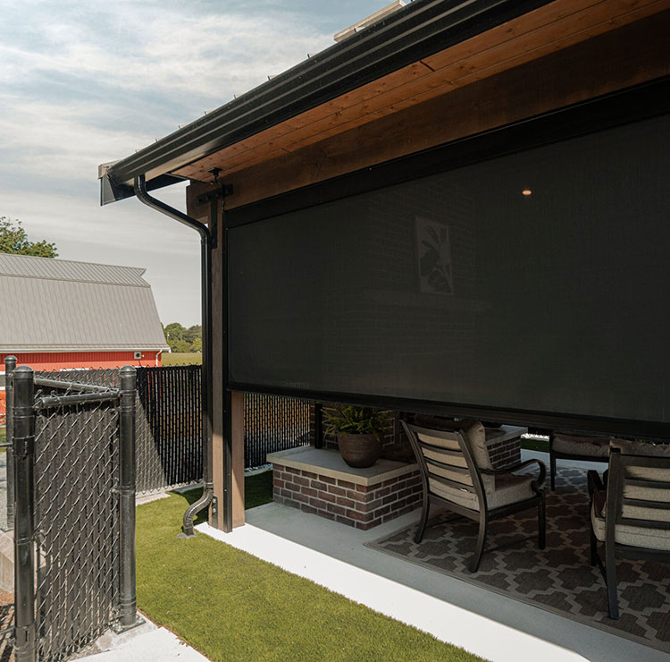 Terrasse couverte avec moustiquaire motorisée foncée, salon extérieur et vue sur une grange rouge en arrière-plan