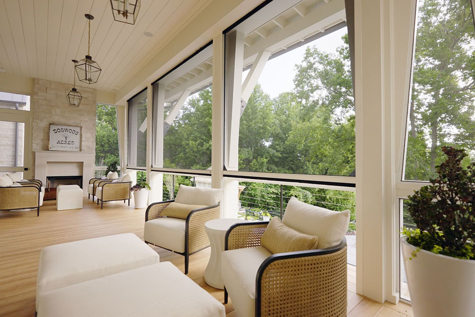 Élégante véranda couverte avec moustiquaires rétractables, plafond blanc, sièges confortables et vues panoramiques sur les arbres et la verdure environnants.