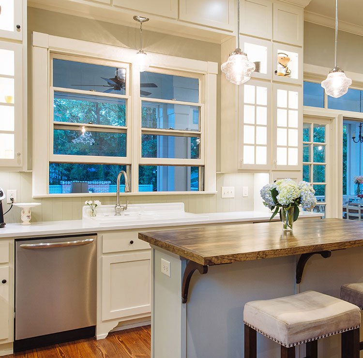 Cuisine lumineuse avec armoires blanches et luminaires suspendus en cristal, avec grandes fenêtres donnant sur le jardin