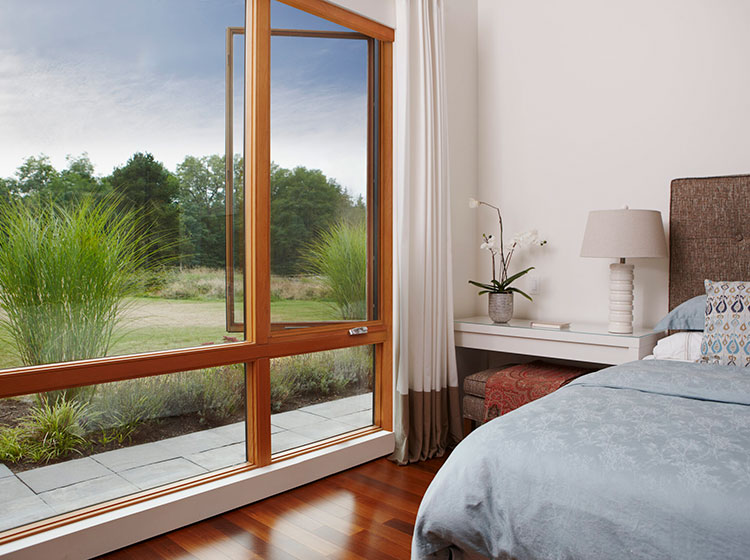 Chambre moderne avec grande fenêtre à cadre en bois surplombant une prairie naturelle, avec parquet et literie élégante